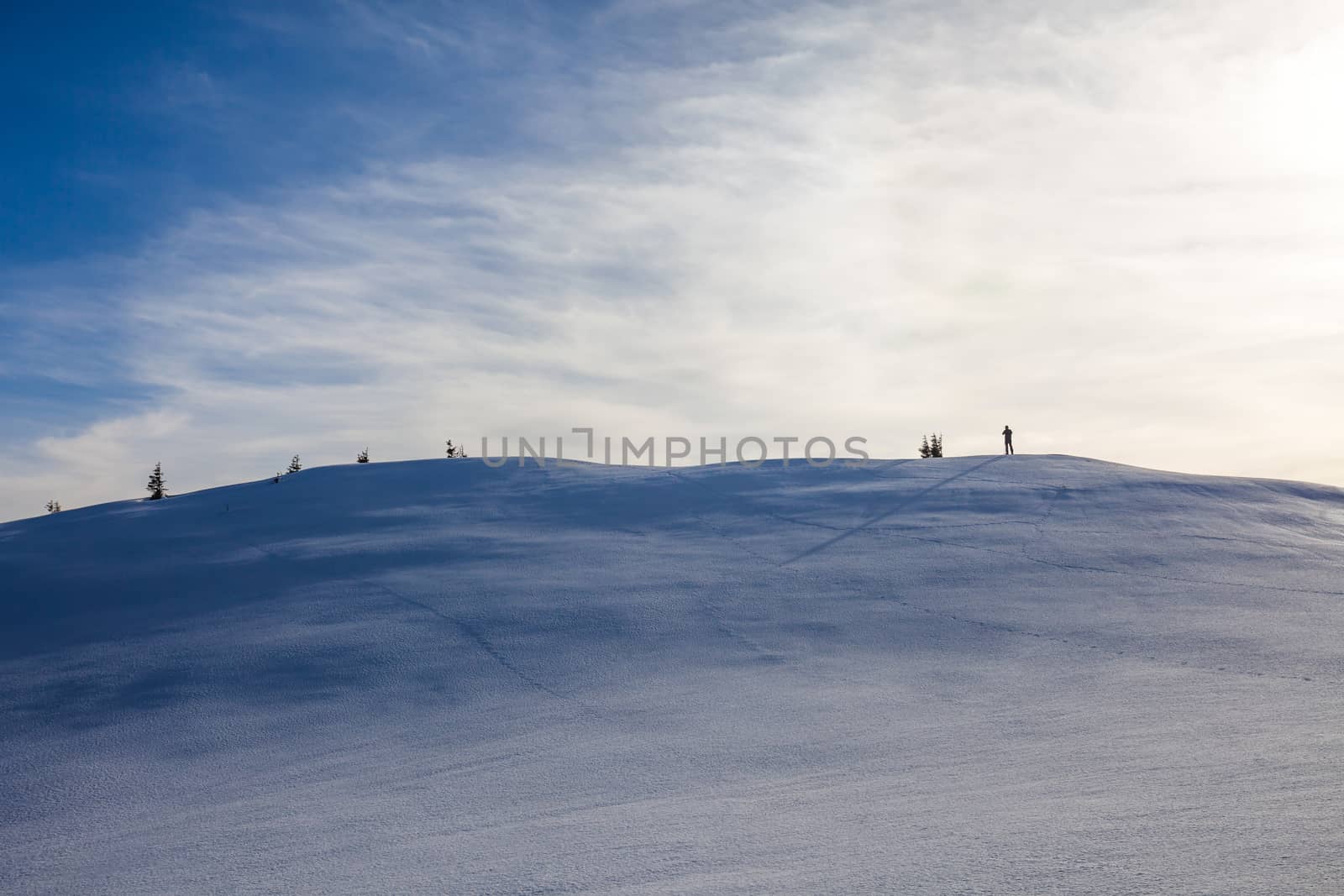 Hiker  with long shadow on top of Mount Ciucas peak on a sunny winter day at sunset, part of Romanian Carpathian Range