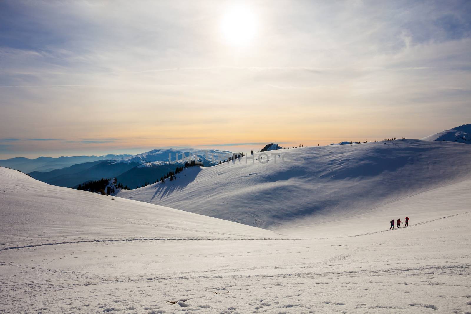 Hikers silhouette at dawn on Mount Ciucas in winter watching the sunset, part of Romanian Carpathian Range