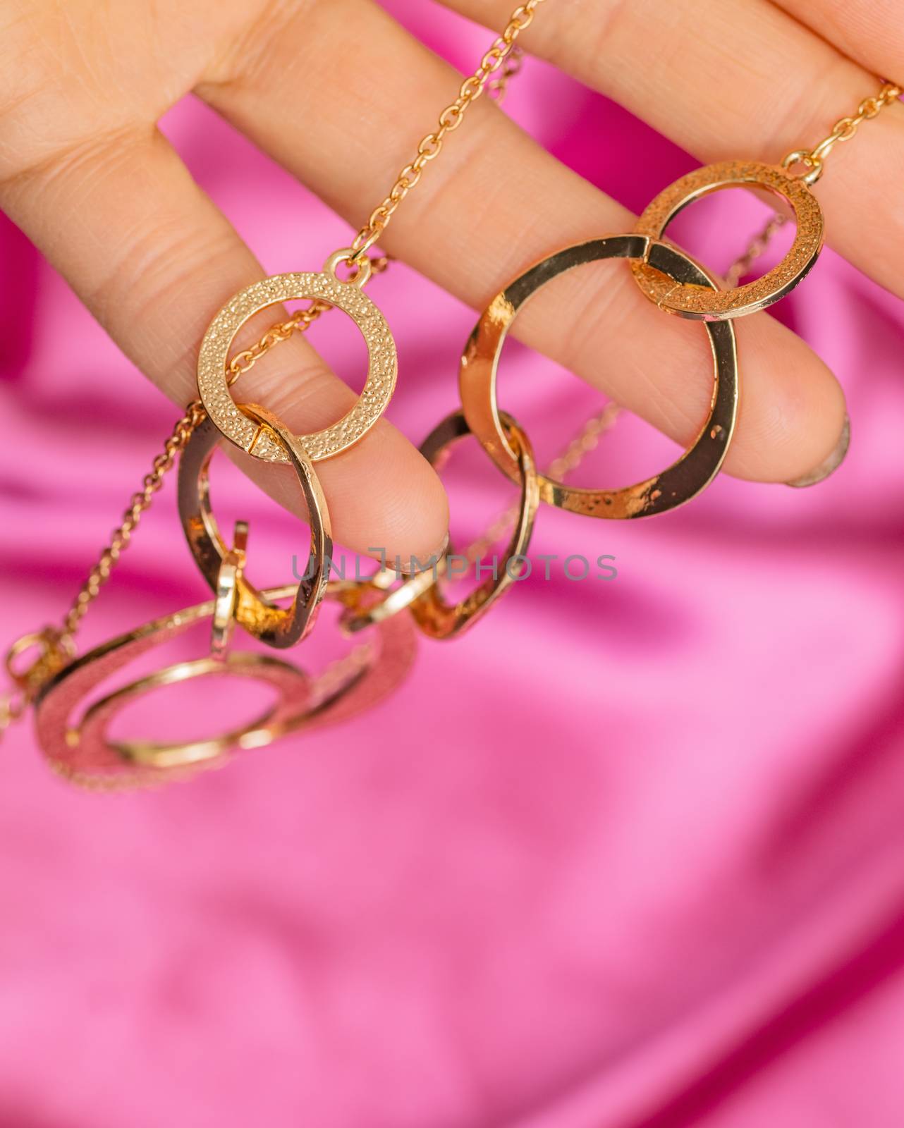 Hand holding Beautiful shiny golden asymmetric necklace with different circle forms over pink background