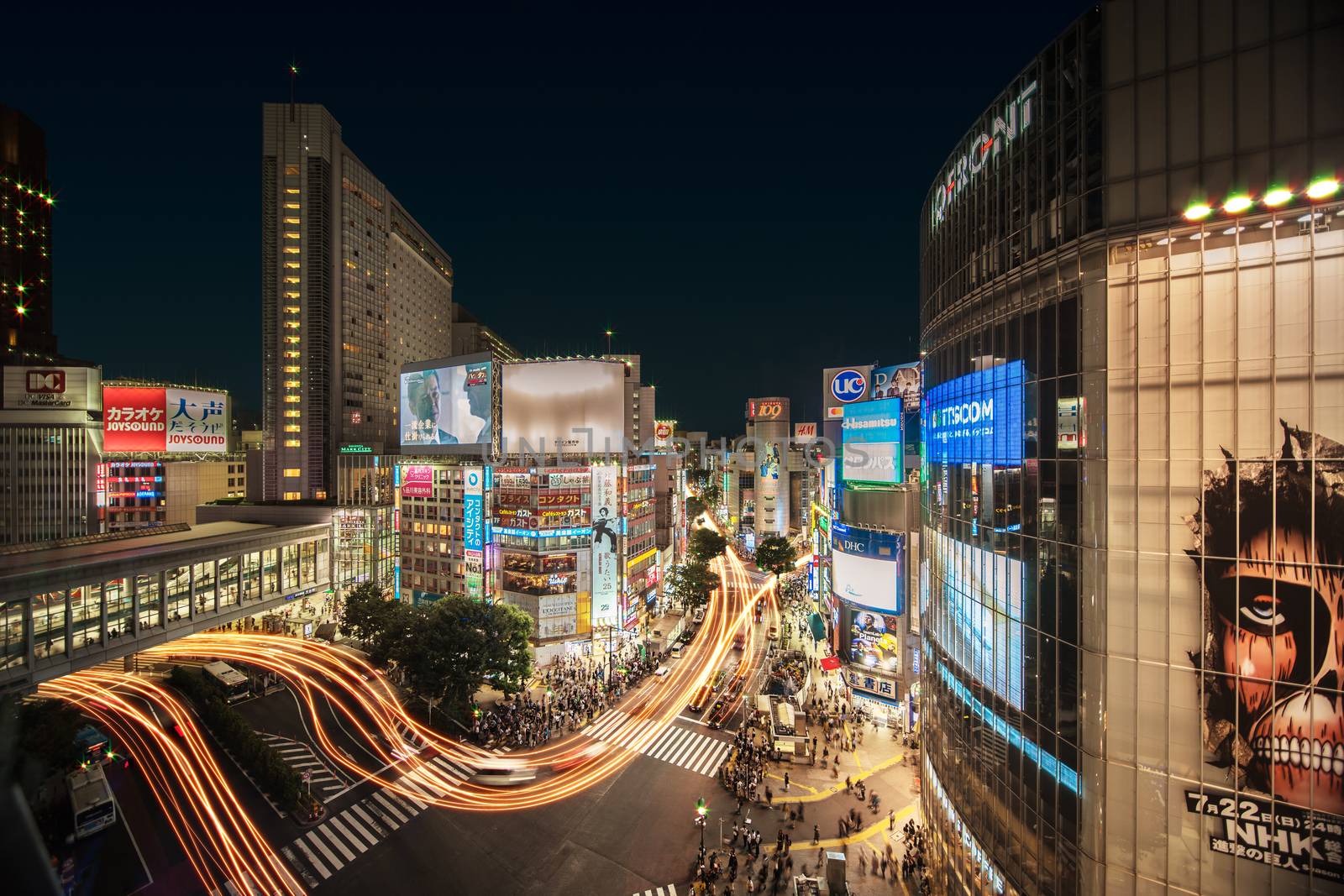 Aerial view of the Shibuya Crossing Intersection in front of Shibuya Station on a summer night with the speed lights flow of cars.