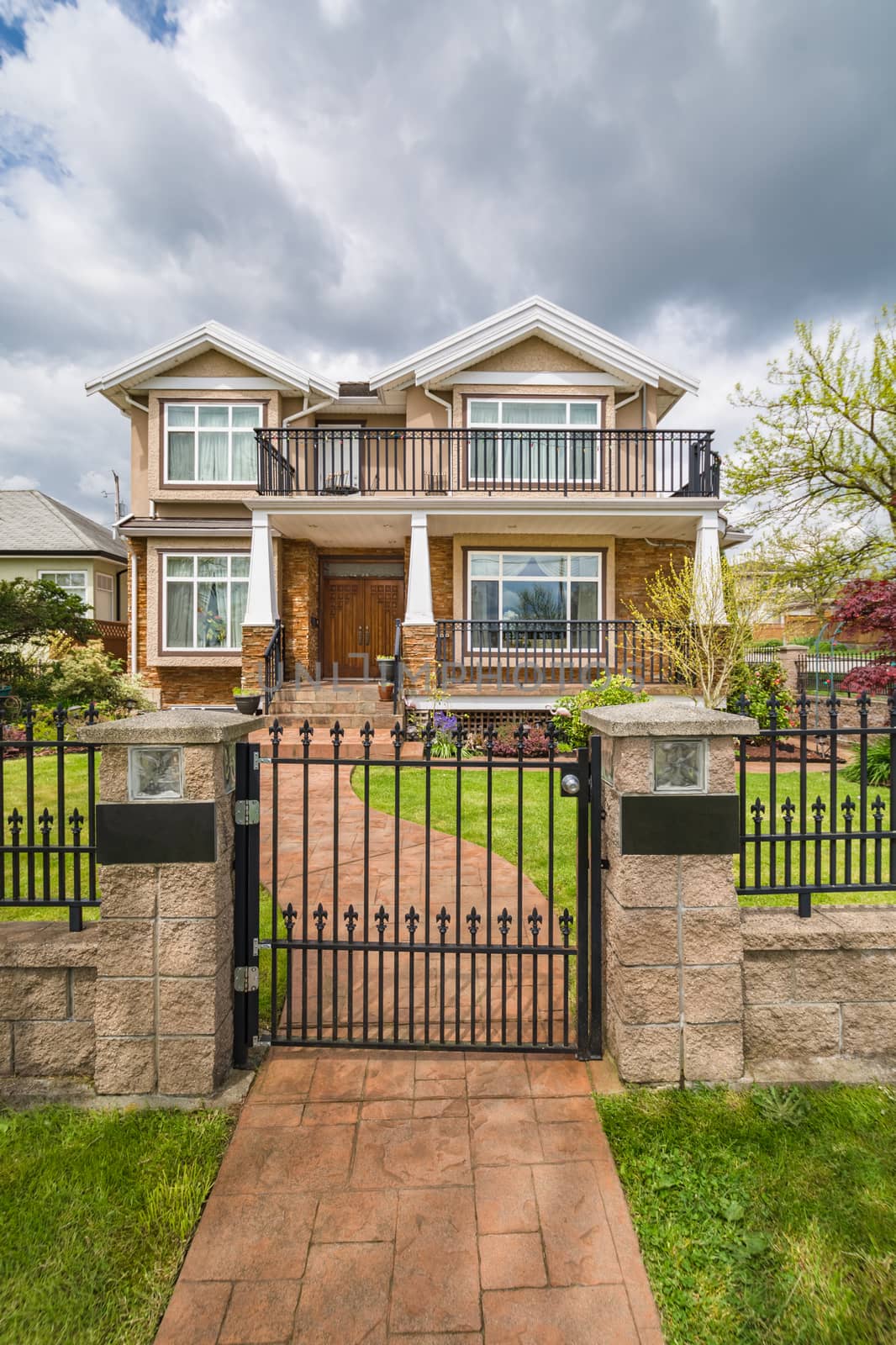 Luxury residential house with green lawn on the front yard behind metal fence