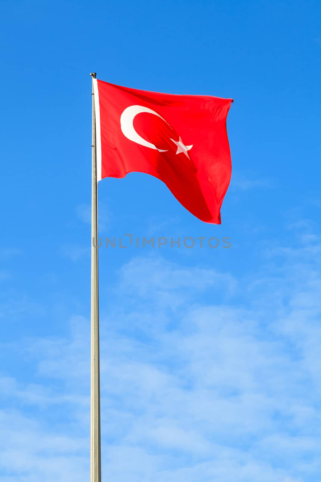 A Turkish flag flying from a flag pole on a beautiful sunny day.