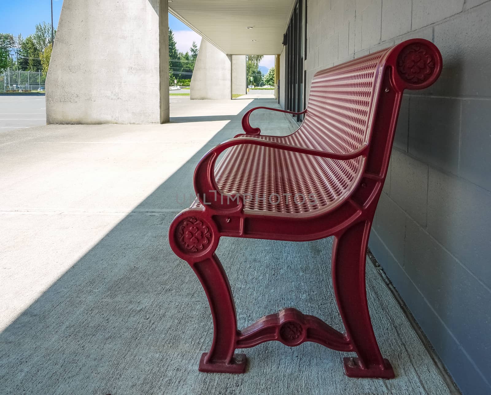 Red metal bench on concrete pavement in shadow of the building on sunny day