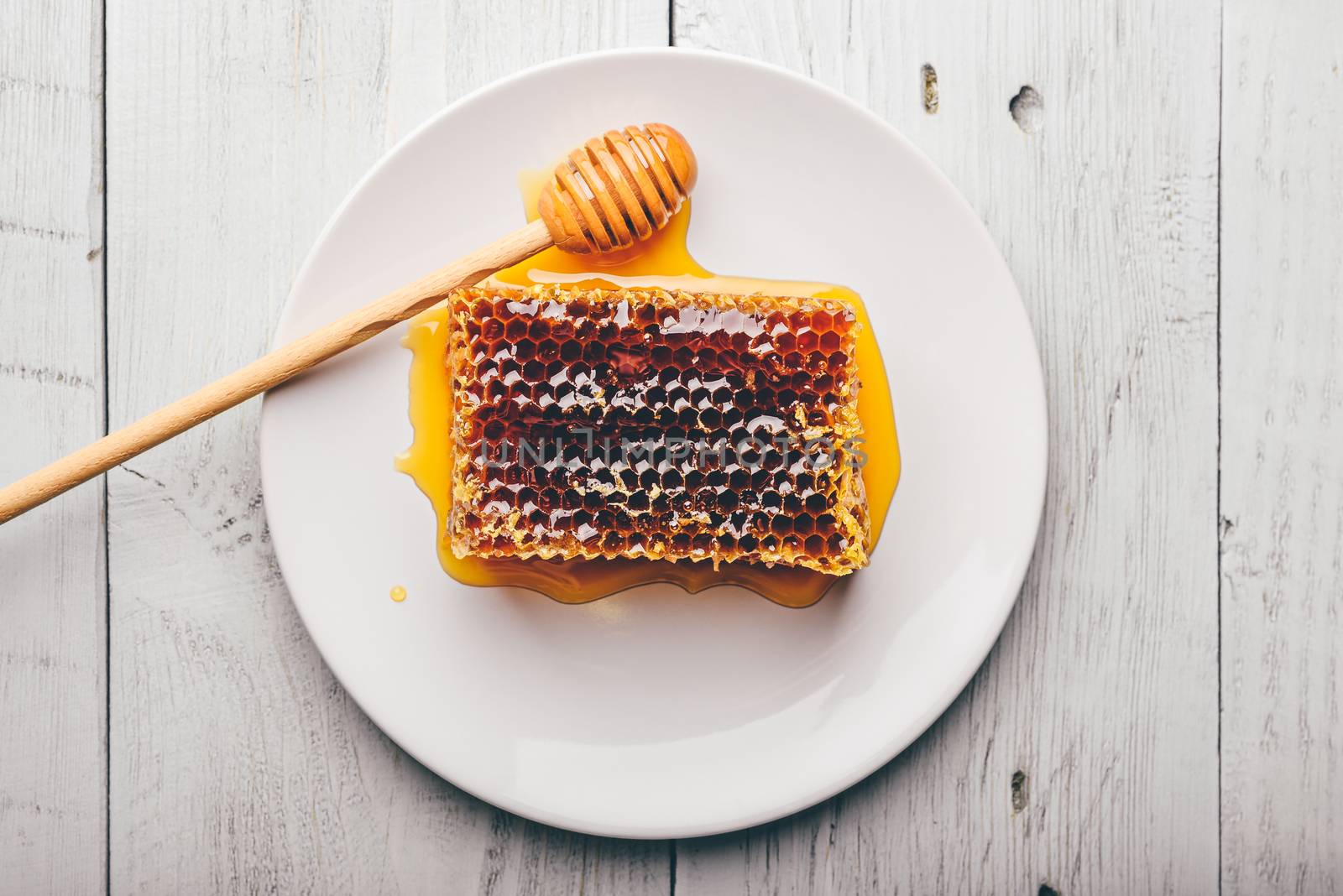 Top view of delicious yummy honeycomb on bright plate with honey dipper over light wooden background