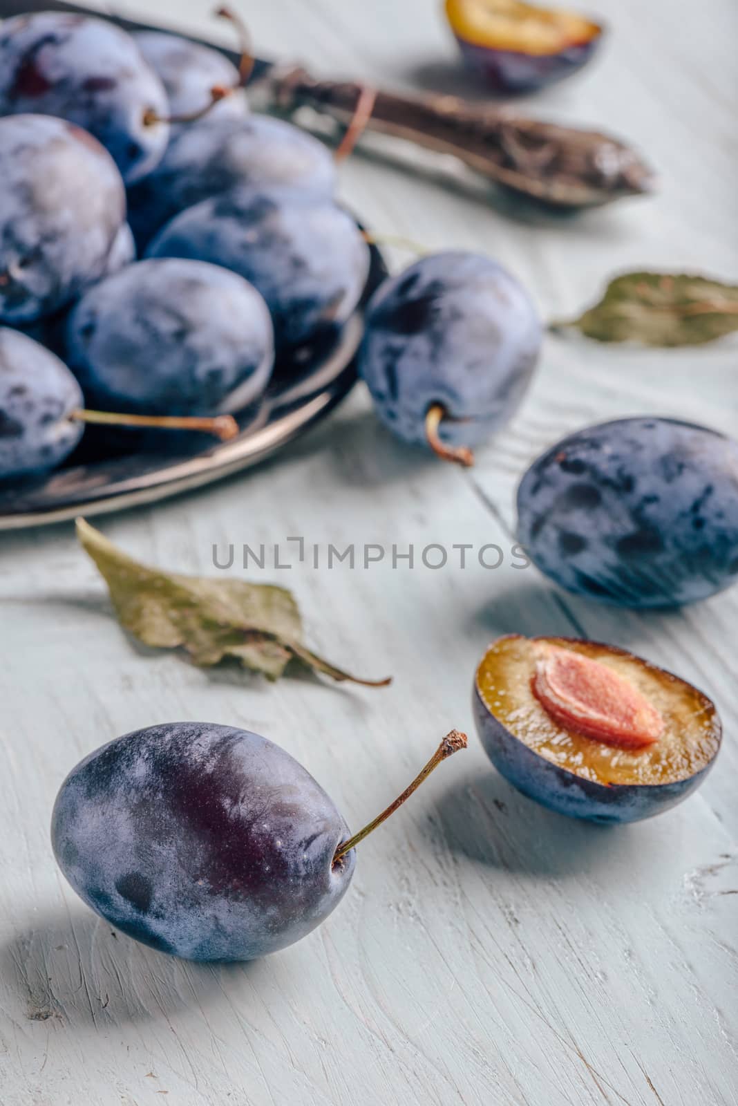 Plums with leaves and knife over wooden surface by Seva_blsv