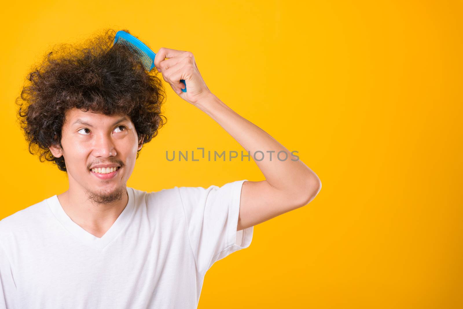 Asian man combing curly hair on yellow background with copy space for text