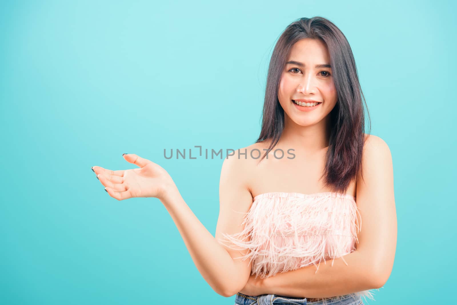 Smiling face Asian beautiful woman her showing hand something near body on blue background, with copy space for text
