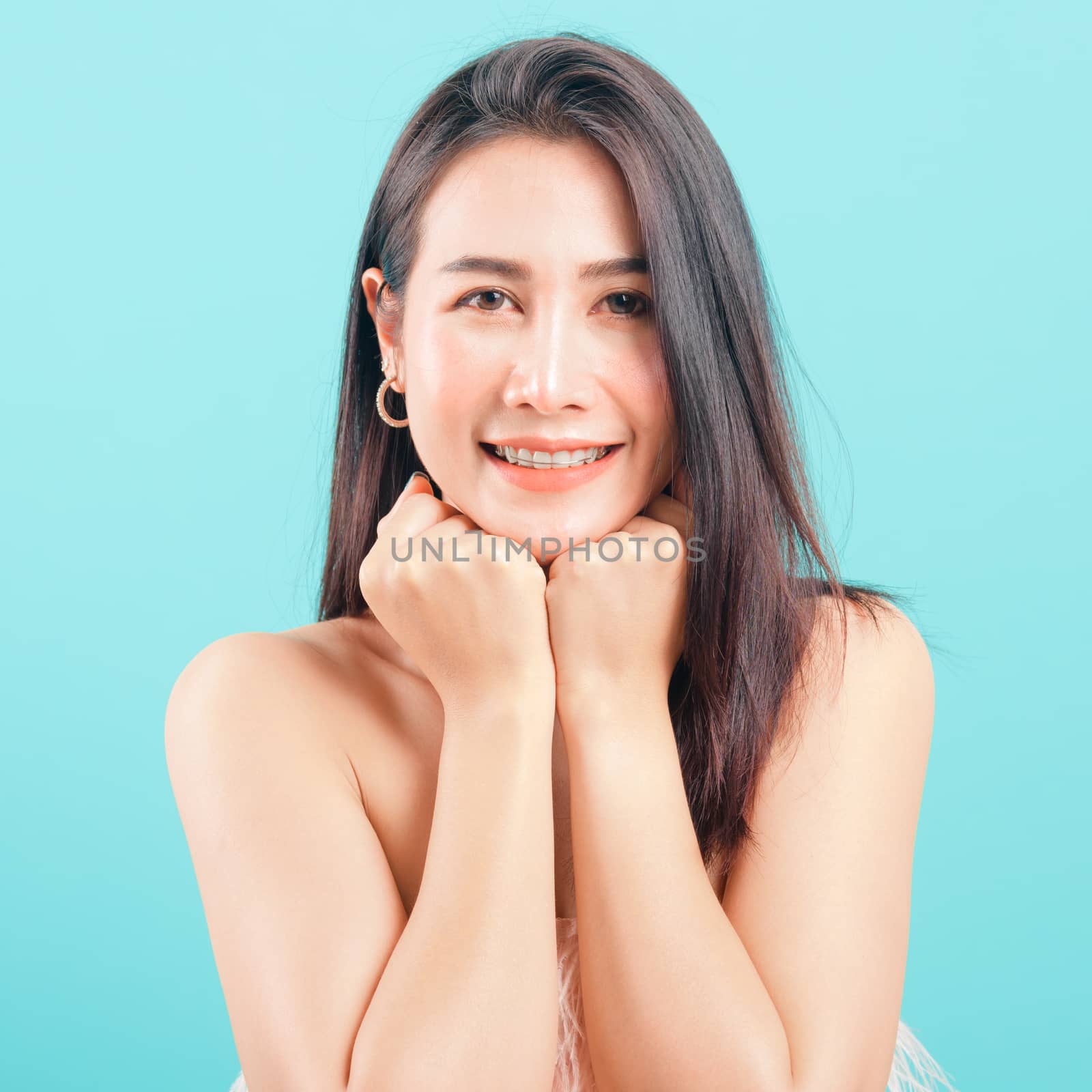 Smiling face Asian beautiful woman her glad keeps both hands under chin smiles pleasantly on blue background