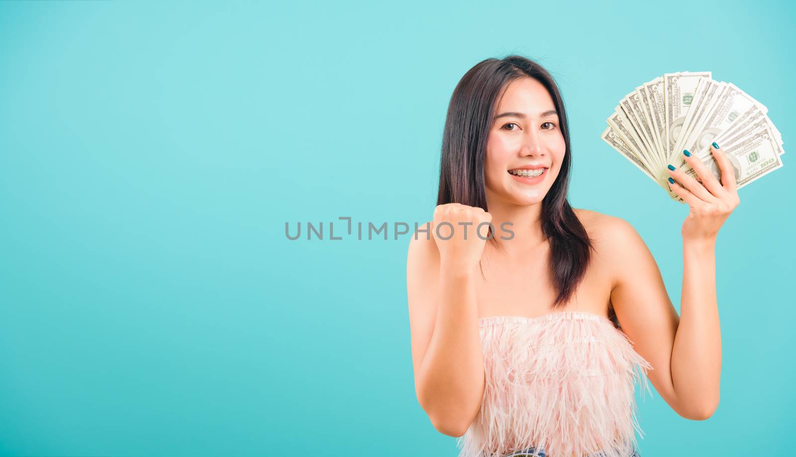 Smiling face portrait asian beautiful woman cheerful her holding money and her looking to camera on blue background, with copy space for text