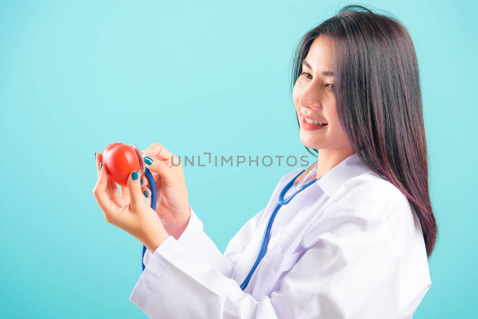 Portrait asian beautiful doctor woman smiling her standing with stethoscope examining red heart on blue background, with copy space for text