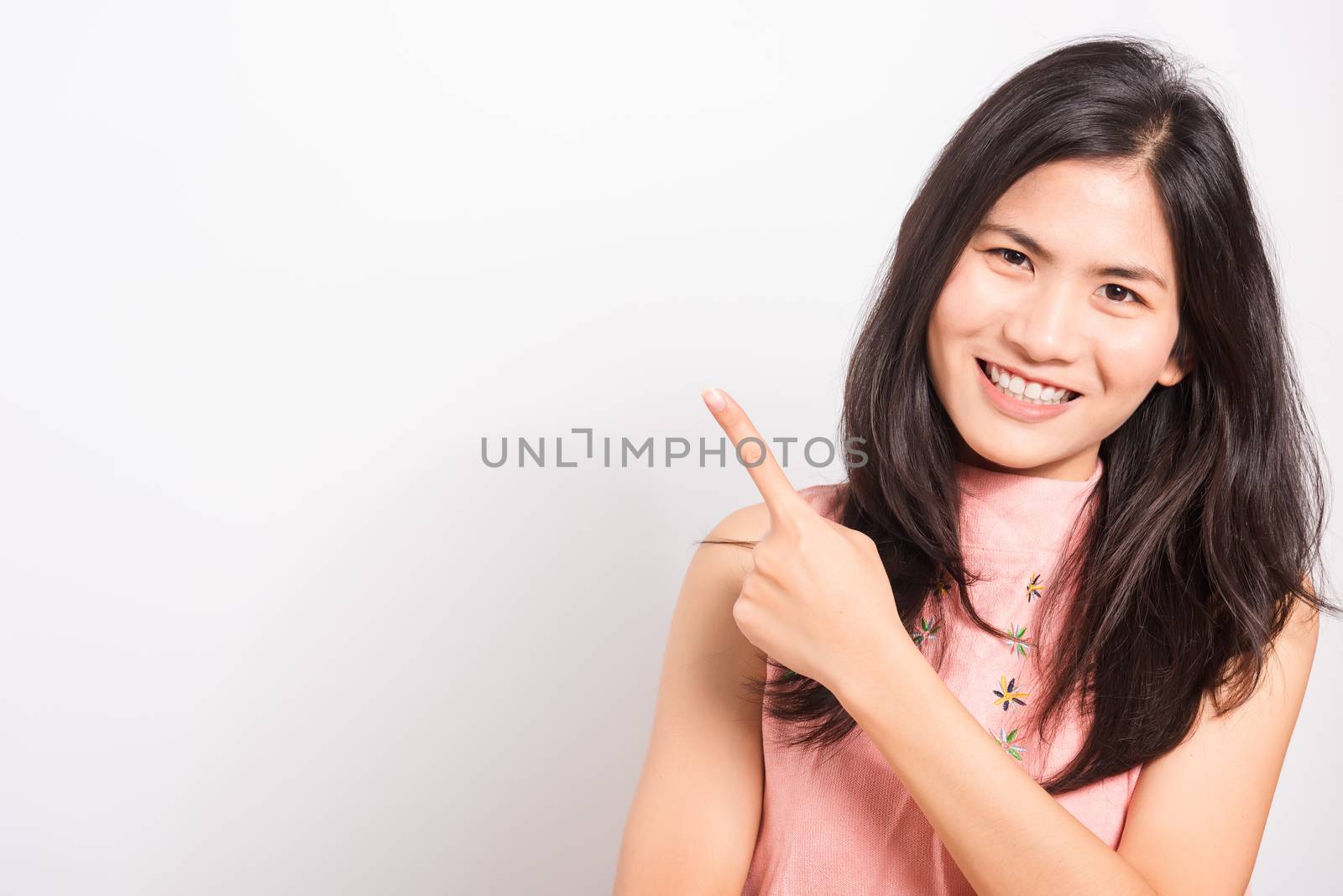 Portrait Asian beautiful young woman standing smile seeing white teeth, She pointing finger up and looking at camera, shoot photo in studio on white background. There was copy space to put text