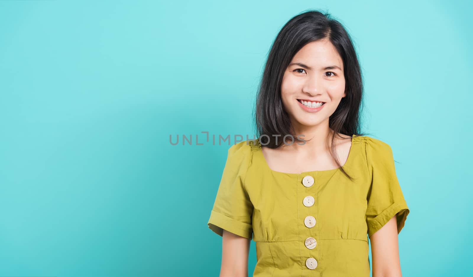 Portrait Asian beautiful young woman standing smile seeing white teeth, She looking at the camera, shoot photo in studio on blue background. There was a copy space to put text on the left-hand side.