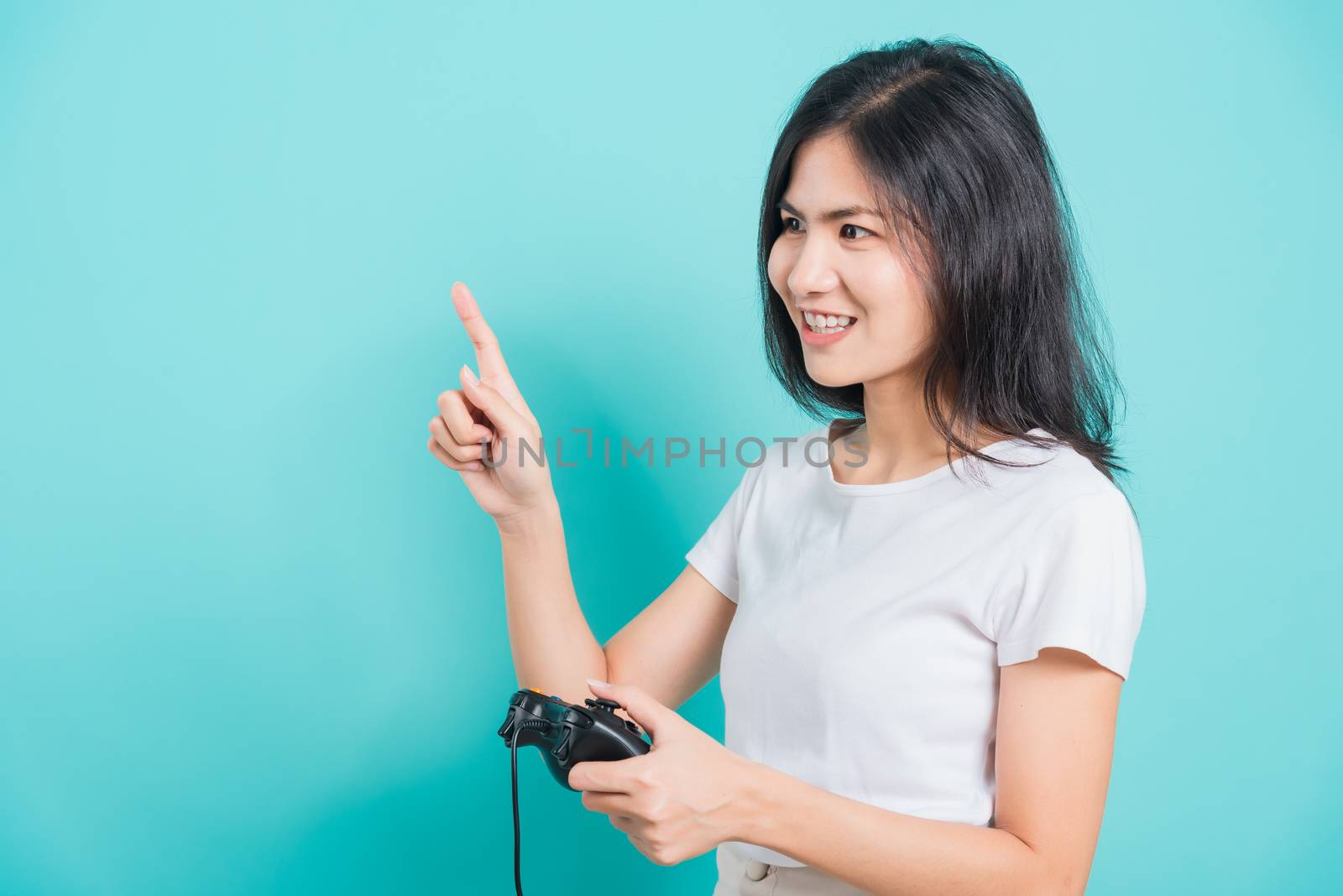 Portrait Asian beautiful happy young woman wear t-shirt gamer with a joystick or gamepad in hands and point finger space, on blue background, with copyspace