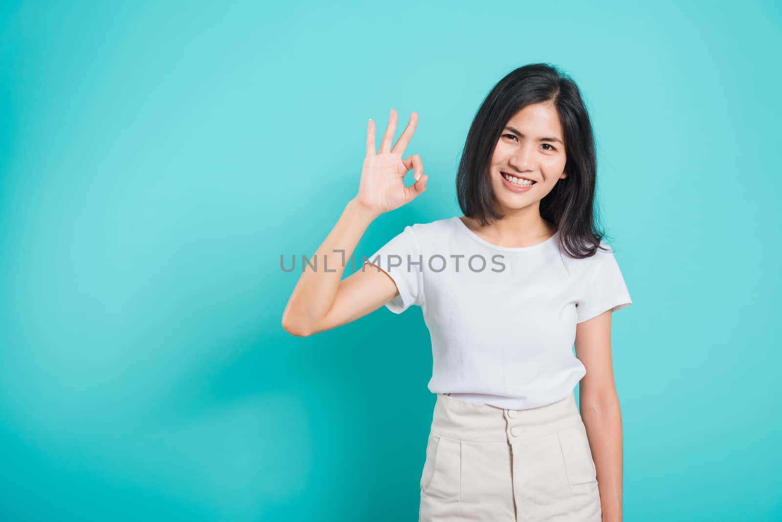 Portrait Asian beautiful young woman standing, She made finger OK symbol sign to agree and looking at camera, shoot photo in studio on blue background, There was copy space