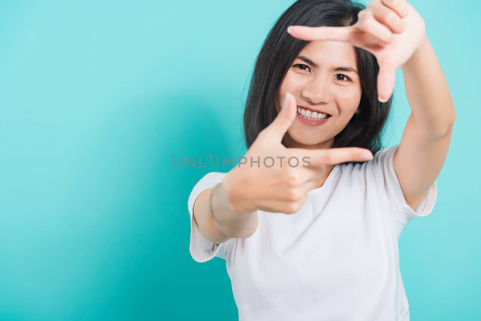 Portrait Asian beautiful happy young woman smile white teeth wear white t-shirt standing making creativity photography frame with hands and fingers, on a blue background with copy space