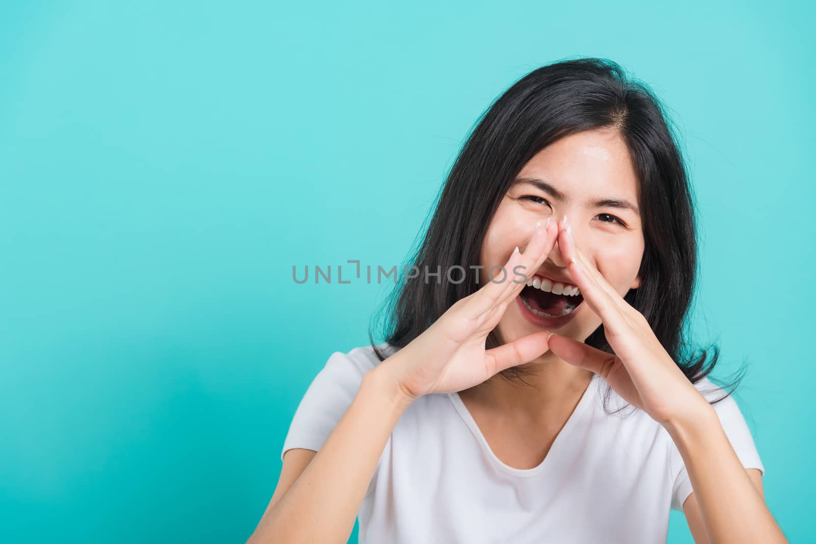 Portrait Asian beautiful happy young woman smile white teeth wear white t-shirt standing shouting with hands cover mouth, on a blue background with copy space