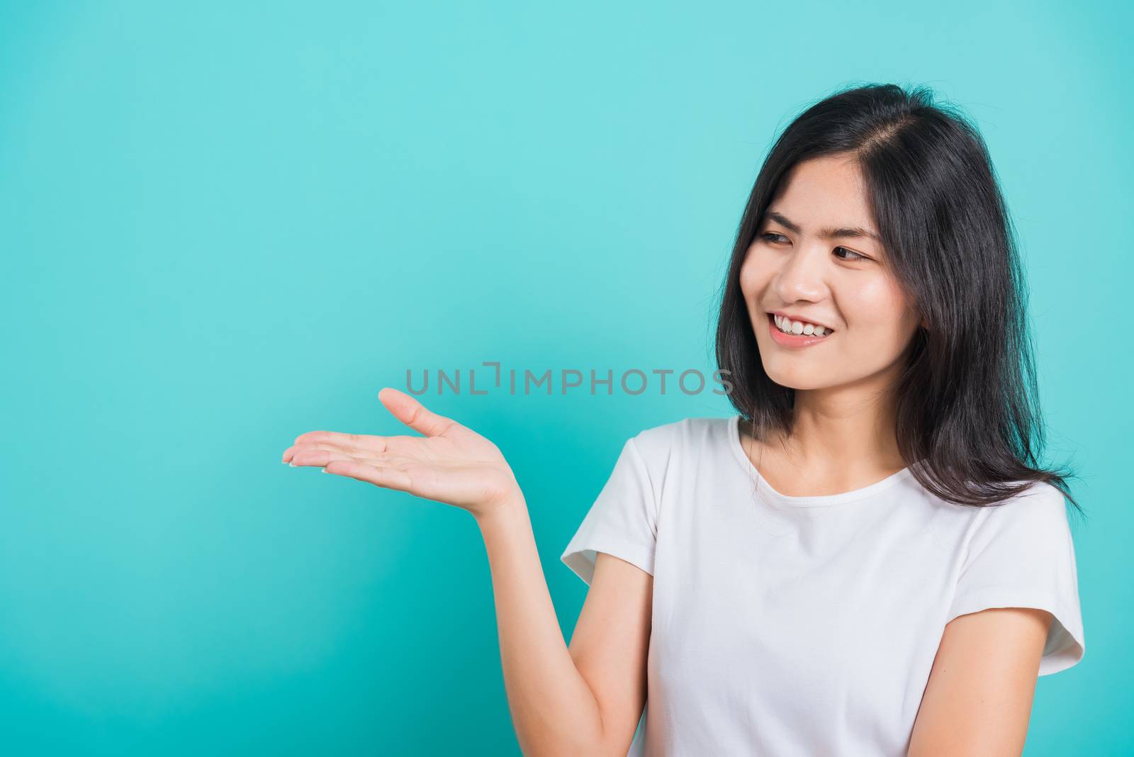 Portrait Asian beautiful young woman standing wear t-shirt, She showing hand to presenting product and looking to product, shoot photo in a studio on blue background, There was copy space