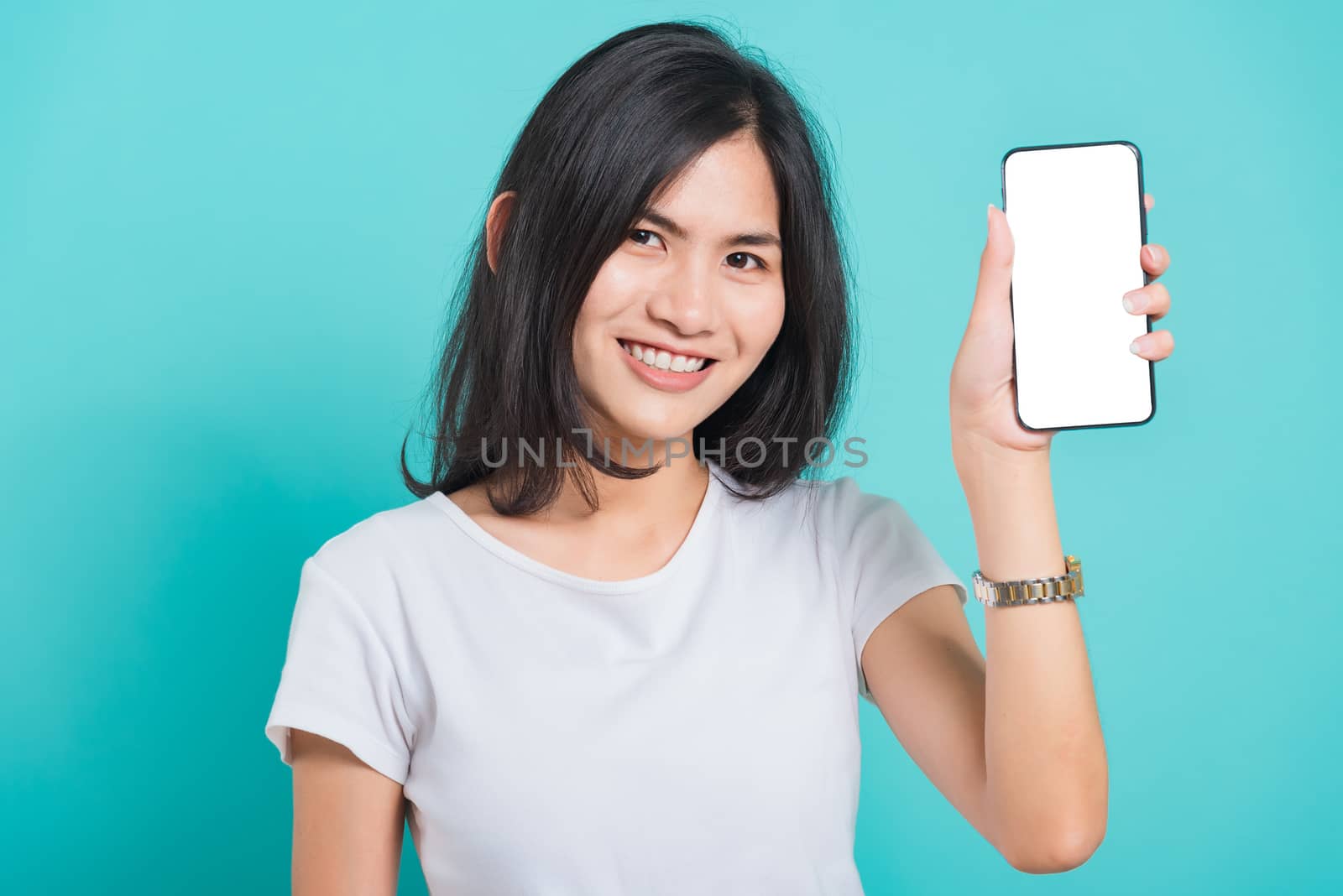 Portrait Asian beautiful happy young woman standing smile showing blank screen mobile phone looking to camera, shoot the photo in a studio on a blue background, There was copy space