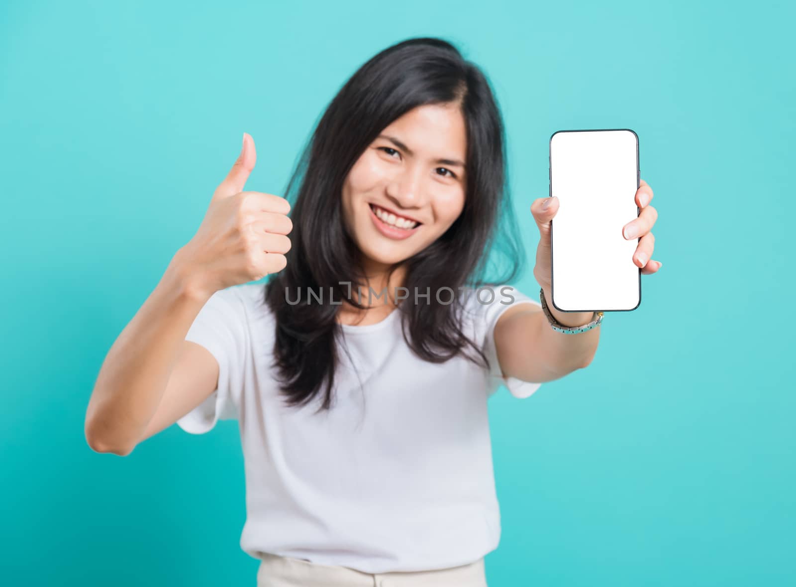 Portrait Asian beautiful happy young woman standing smile, holding blank screen mobile phone and showing thumbs up gesture, shoot photo in studio focus phone on blue background, with copy space