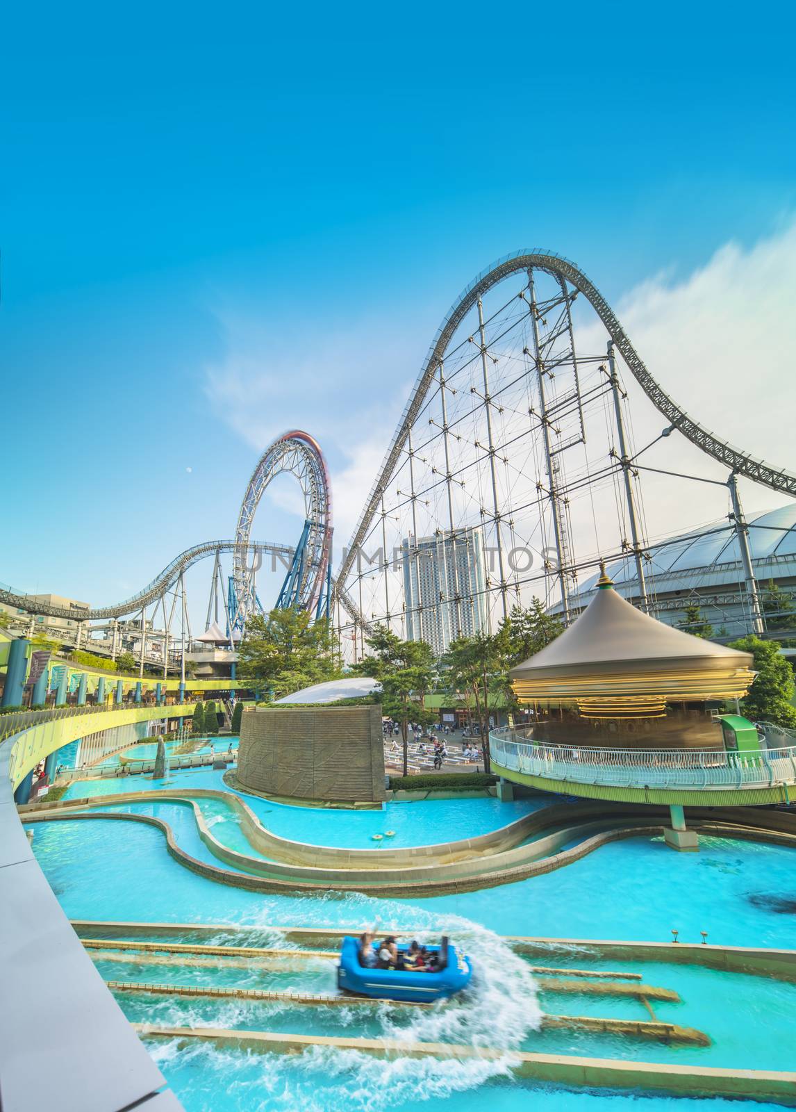 Laqua Tokyo Dome City Mall with its impressive roller coaster integrated in the gallery of its shopping center with a carousel  and water coaster under the summer blue sky.