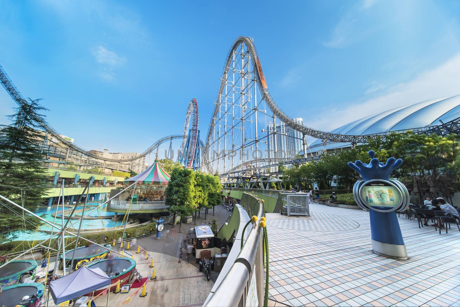 Laqua Tokyo Dome City Mall with its impressive roller coaster integrated in the gallery of its shopping center with a carousel  and water coaster under the summer blue sky.