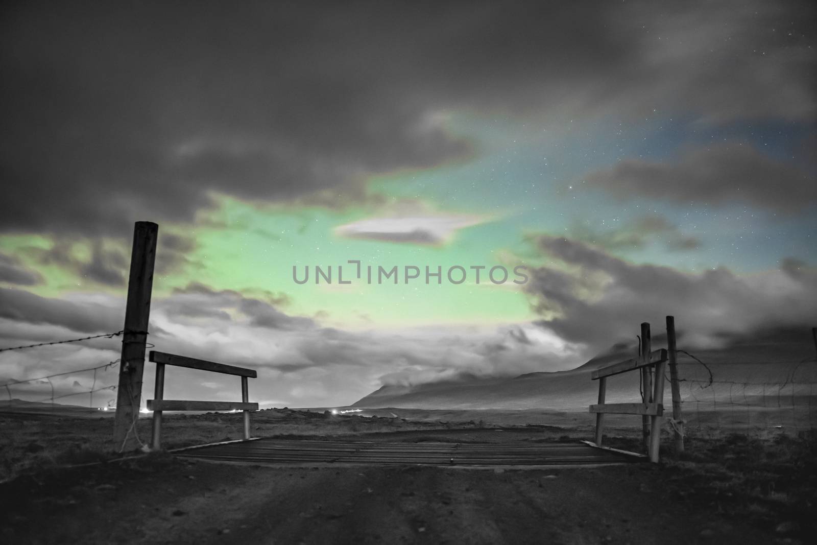 Aurora Borealis in Iceland northern lights shining through gaps in clouds over icelandic farm gate in black white and green by MXW_Stock