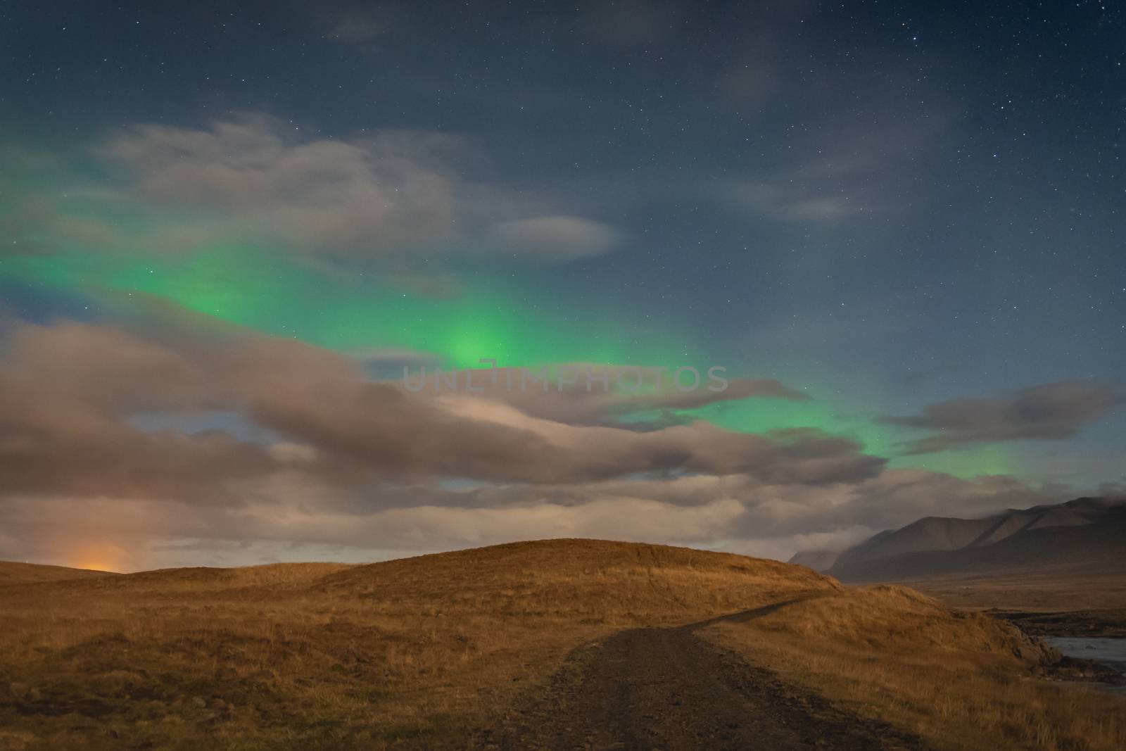 Aurora Borealis in Iceland northern lights shining green over hiking path in Iceland by MXW_Stock