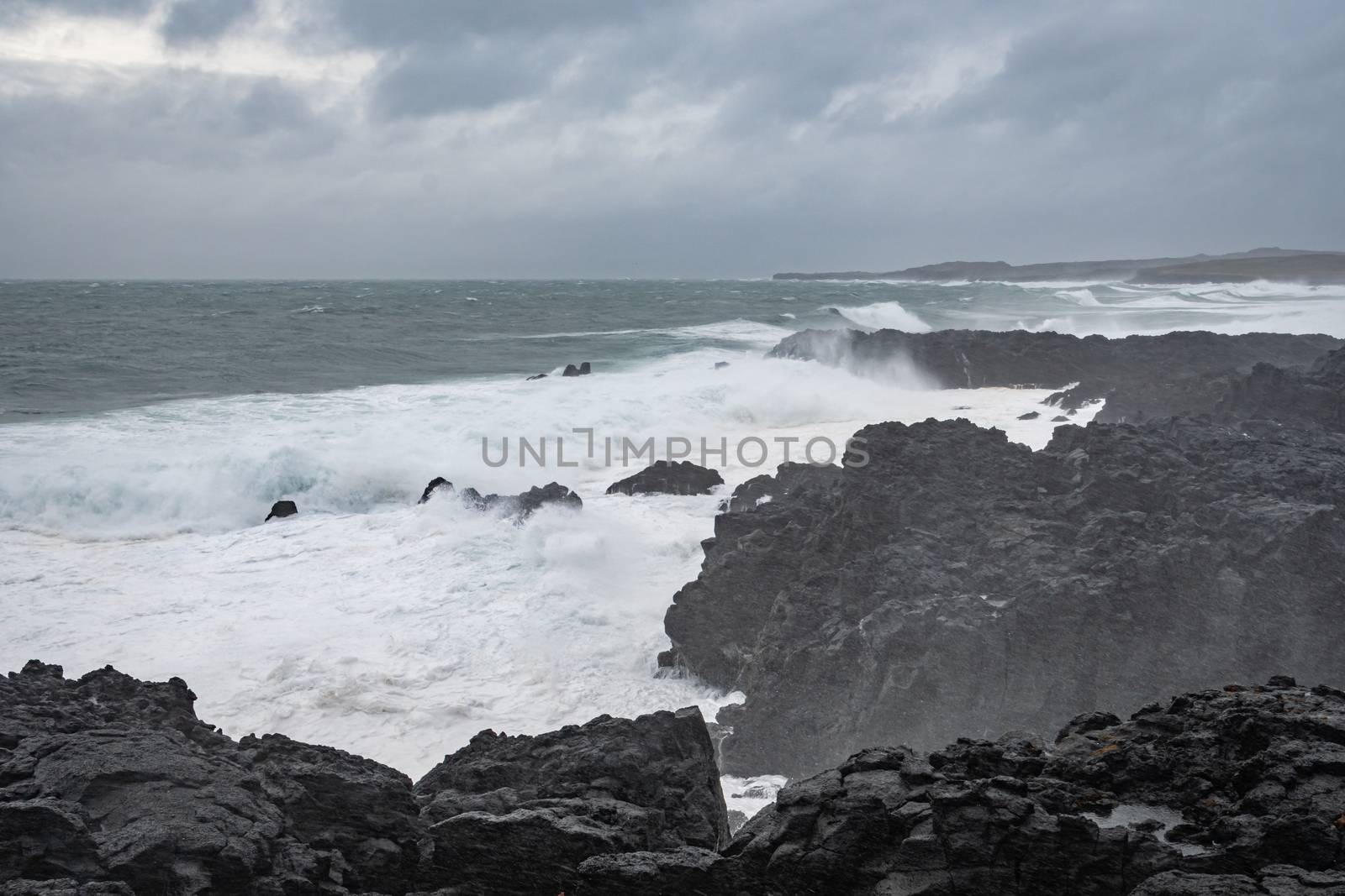 Brimketill lava rock pool in Iceland storm waves hitting black basalt rock by MXW_Stock