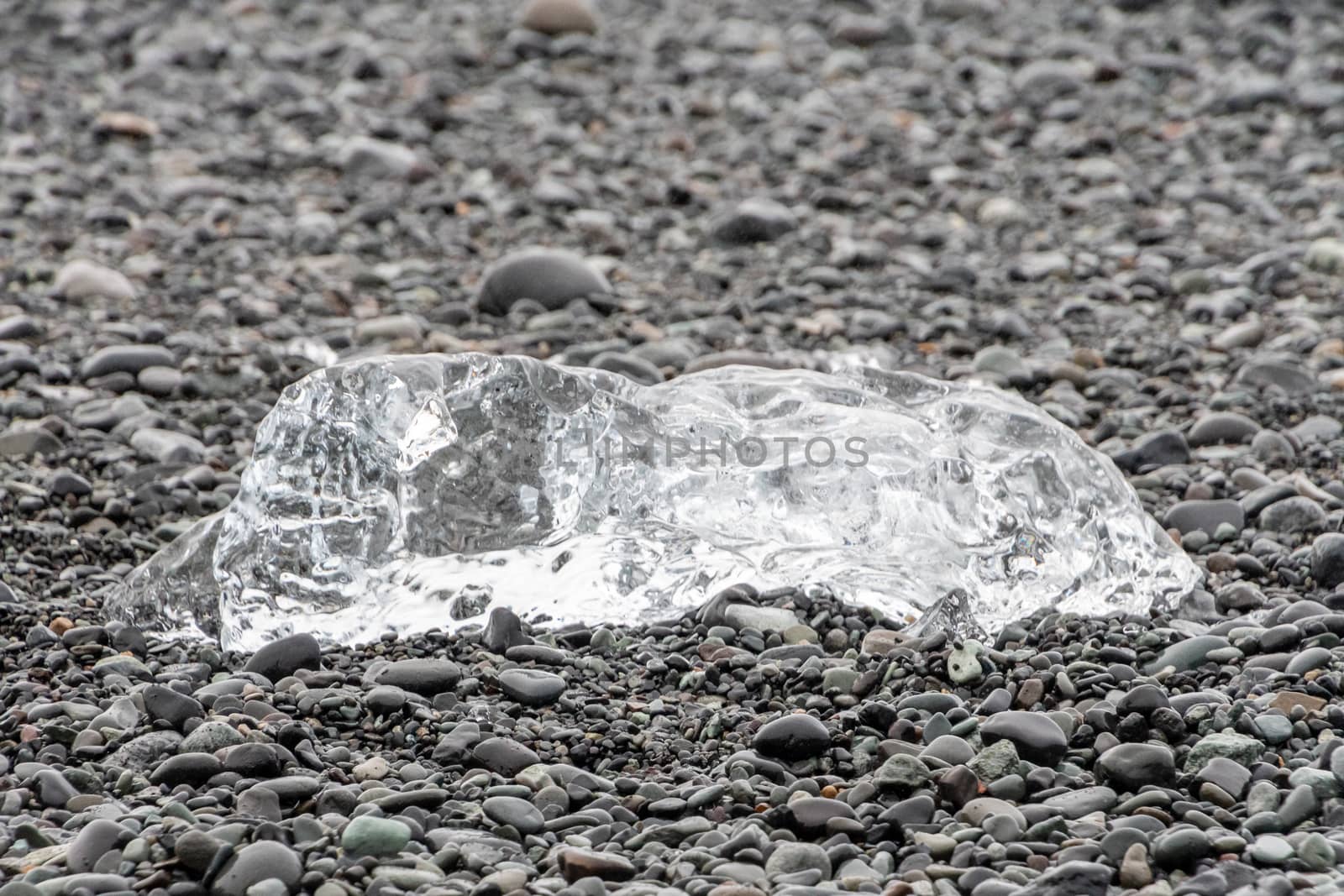 Diamond beach black sand crystal clear piece of ice lying on dark round rocks