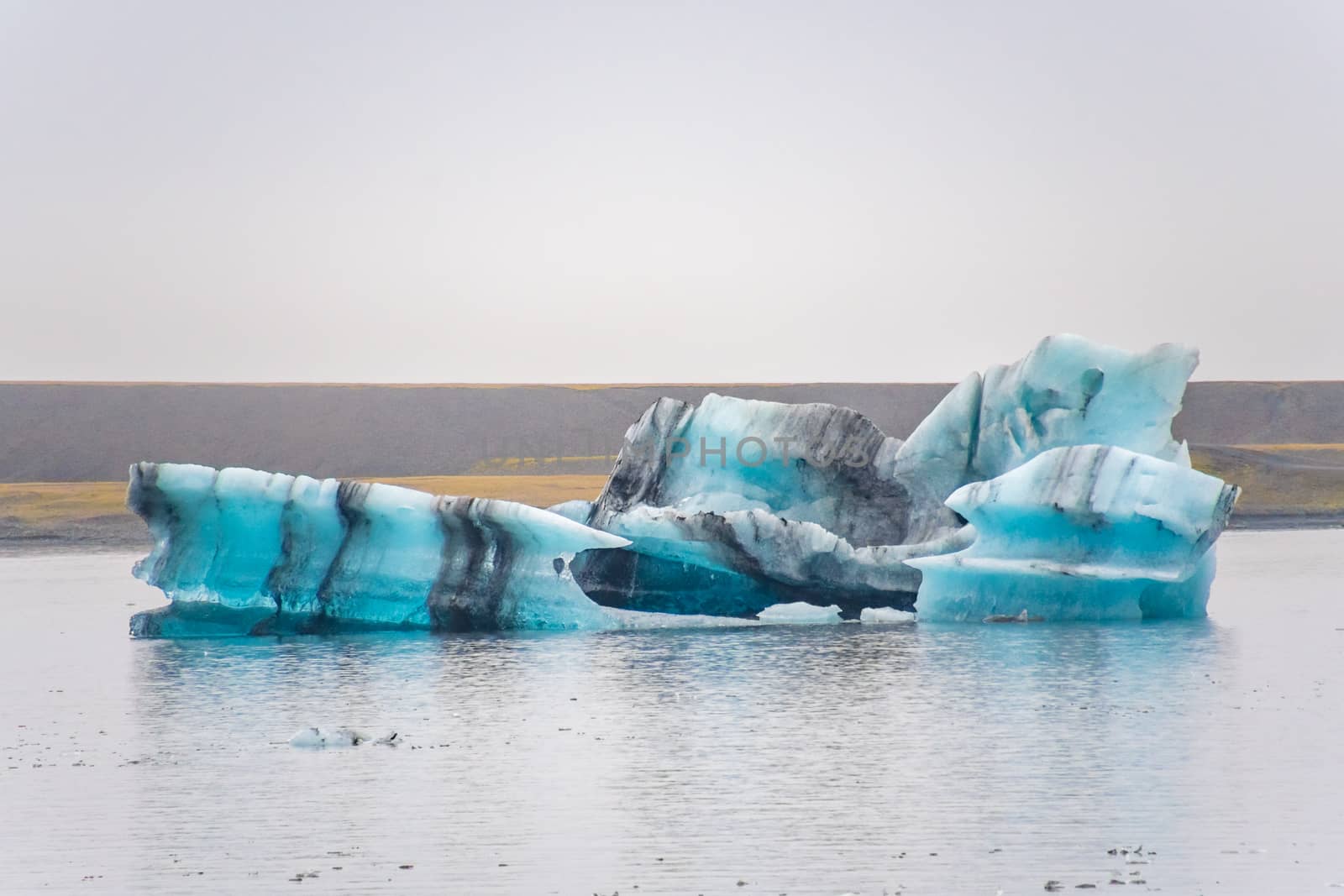 Joekulsarlon Glacier Lagoon deep blue iceberg with dark layers of volcanic ash forming regular pattern
