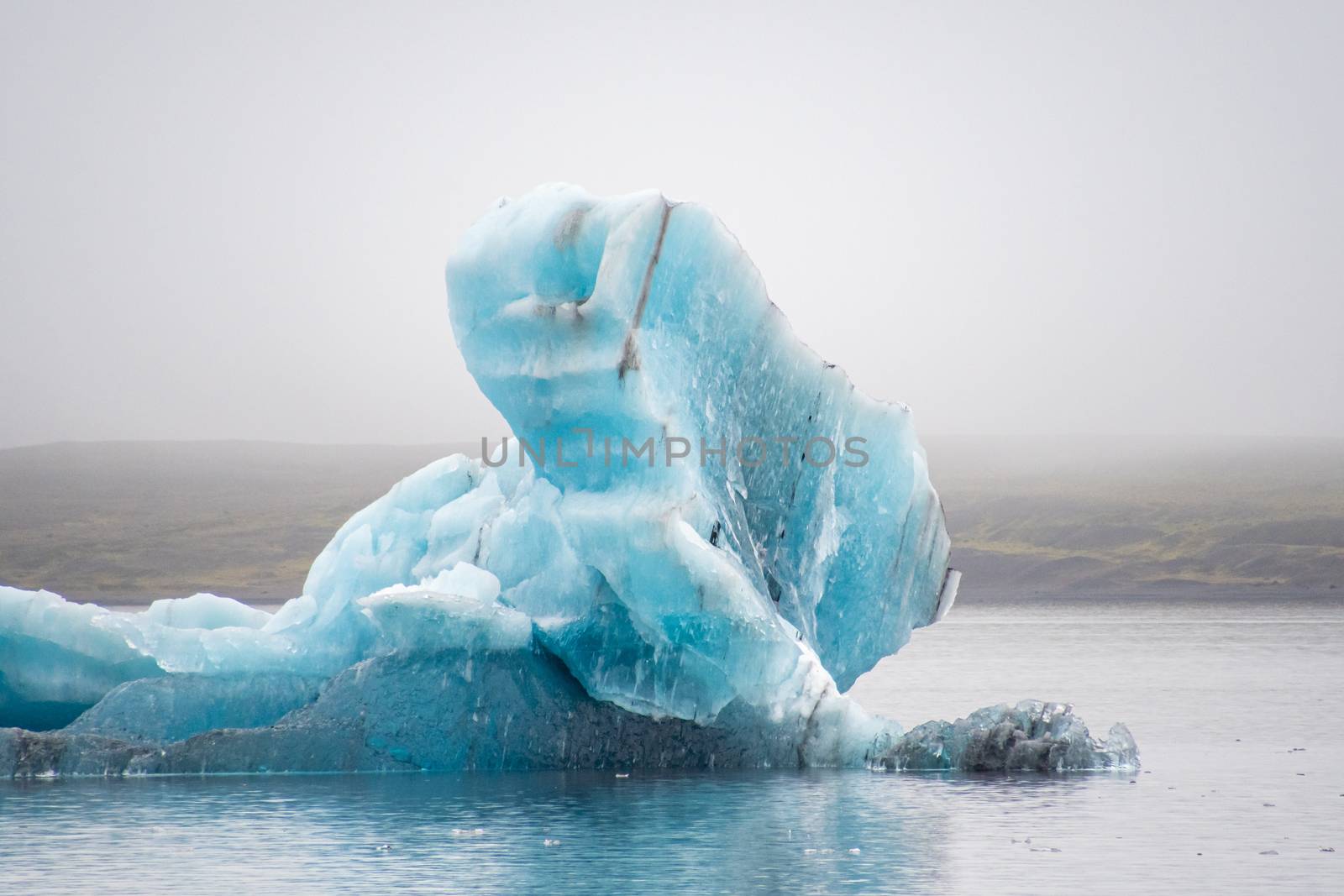 Joekulsarlon Glacier Lagoon deep blue iceberg with dark layers of volcanic ash by MXW_Stock