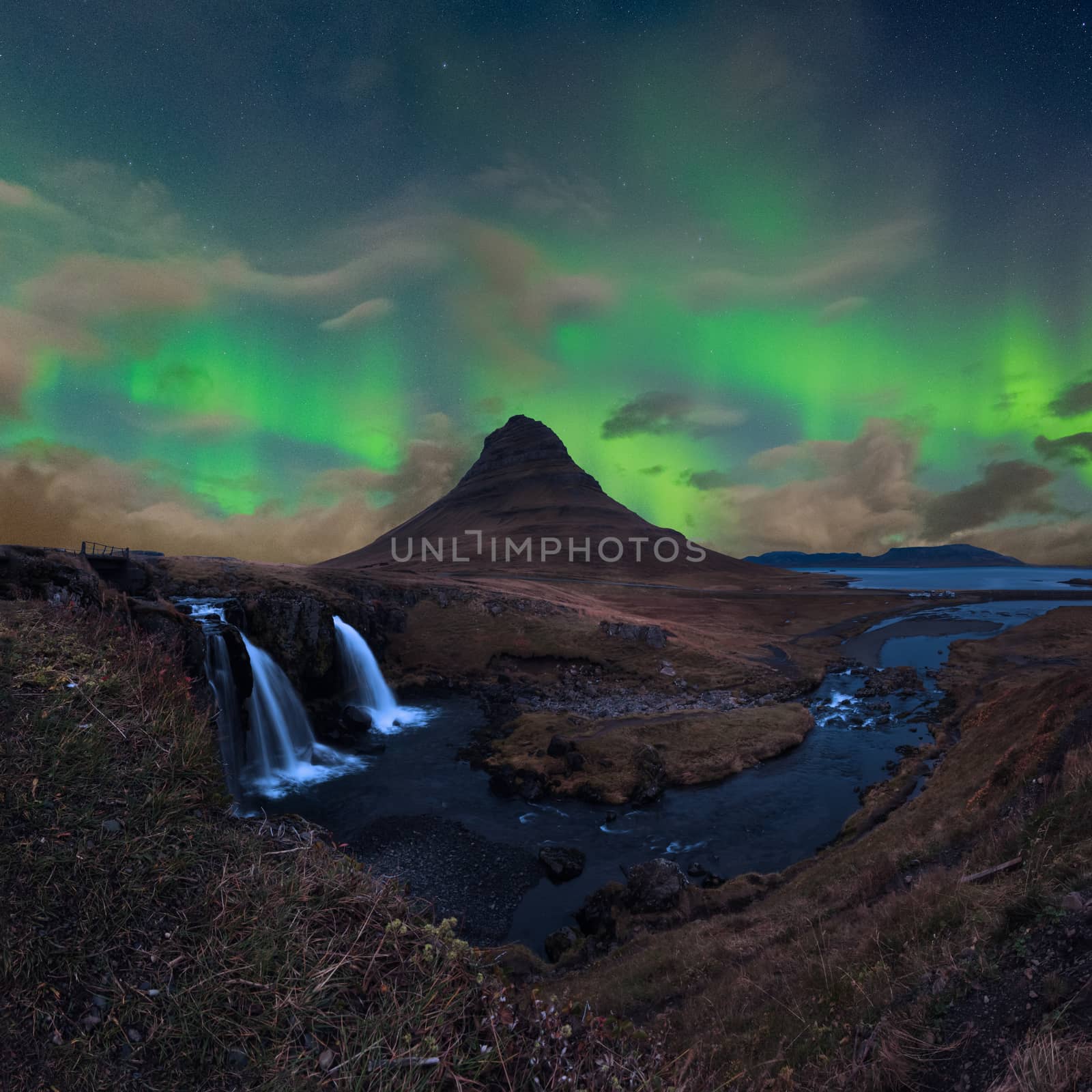 Kirkjufell in Iceland Kirkjufellsfoss waterfall and famous mountain under dancing Aurora by MXW_Stock