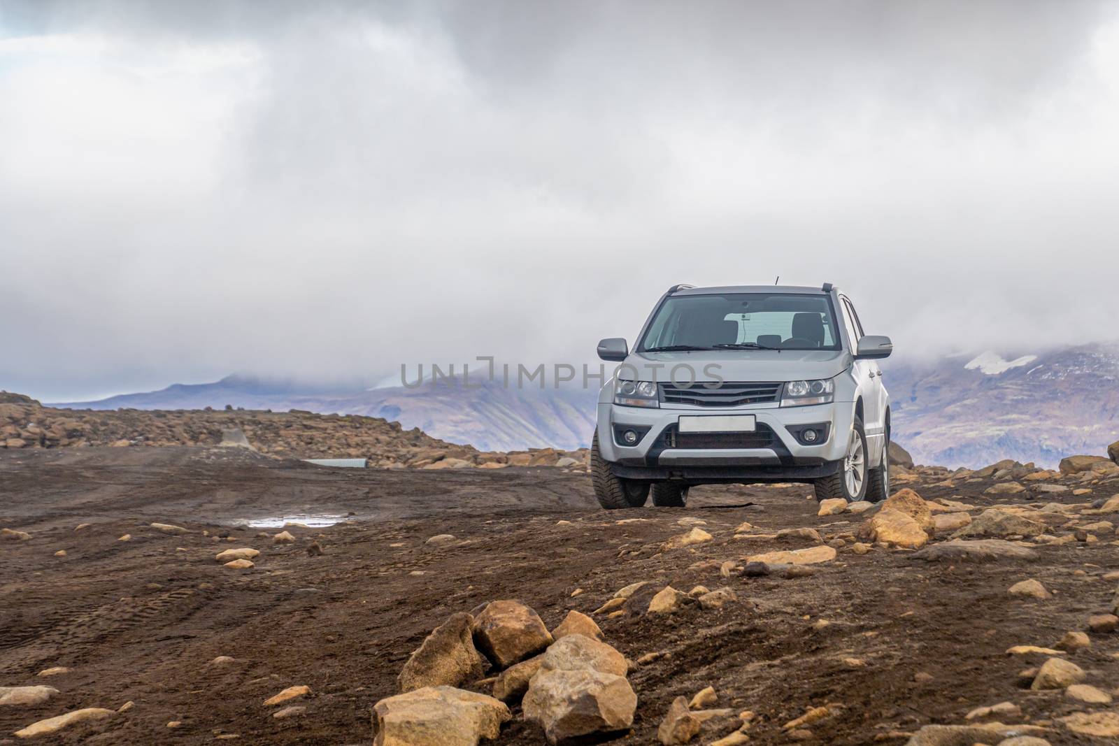 Langjokull Glacier SUV on muddy road standing between rocks in front of mountains by MXW_Stock
