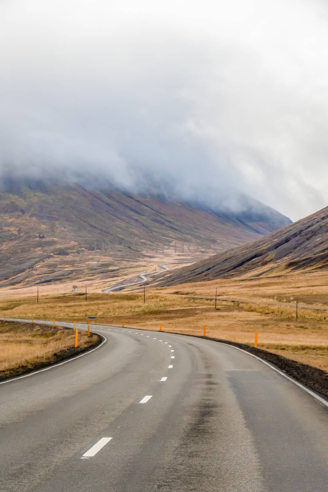 Northern Iceland empty road winding through valley upwards a mountain during grey weather by MXW_Stock