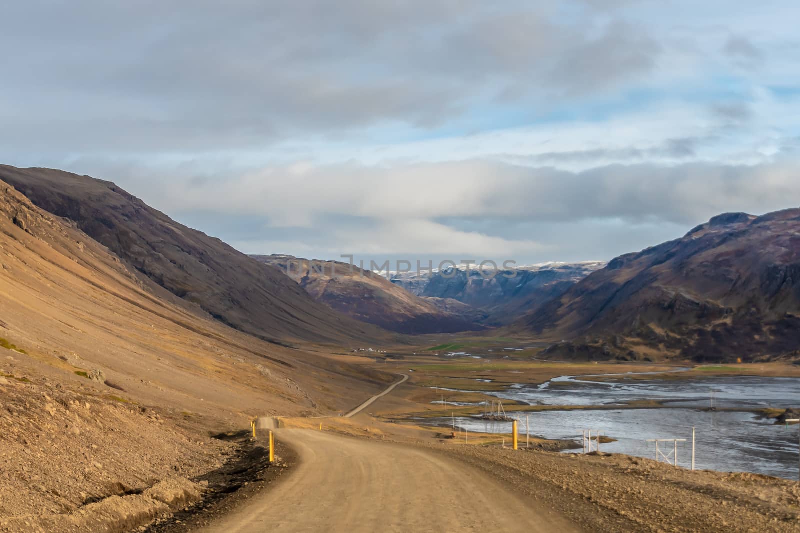 Roadtrip in Iceland dirt road in west iceland winding down into fjord during sunny weather by MXW_Stock