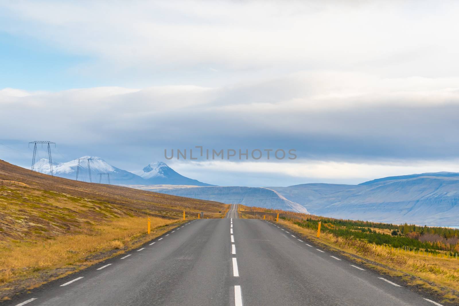 Roadtrip in Iceland empty paved road leading over mountains with snow covered tips next to power line in fall