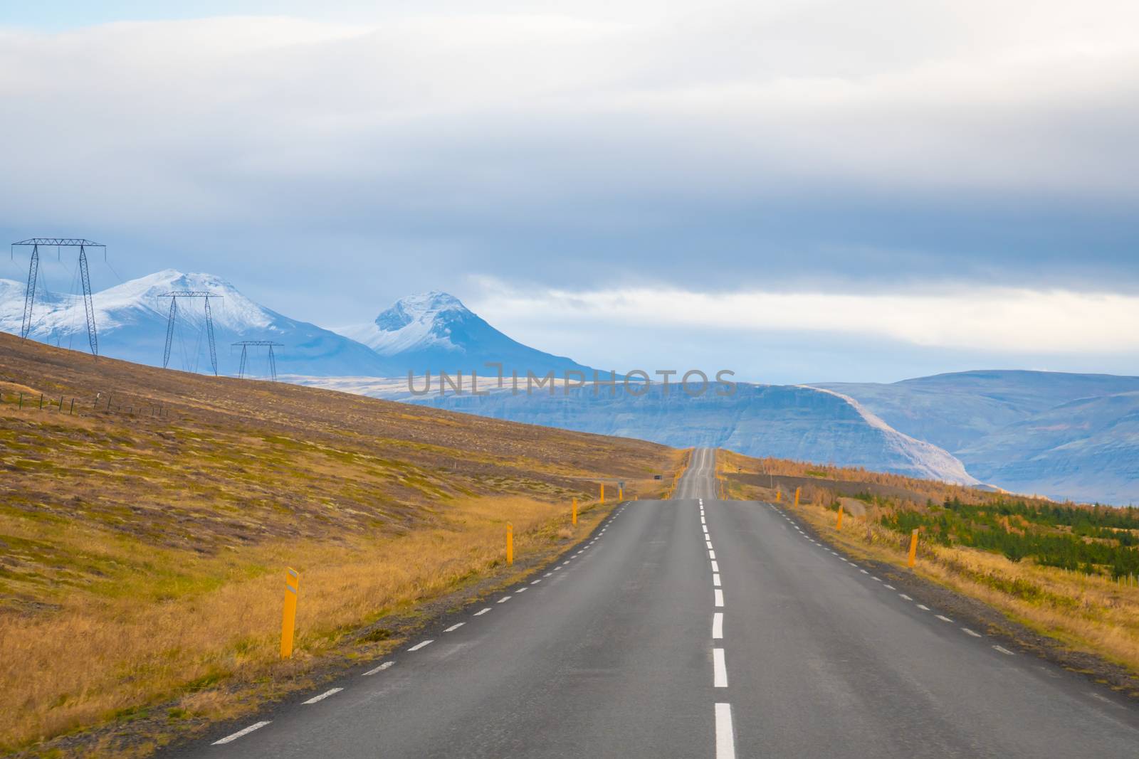 Roadtrip in Iceland empty paved road leading over mountains with snow covered tips next to power lines