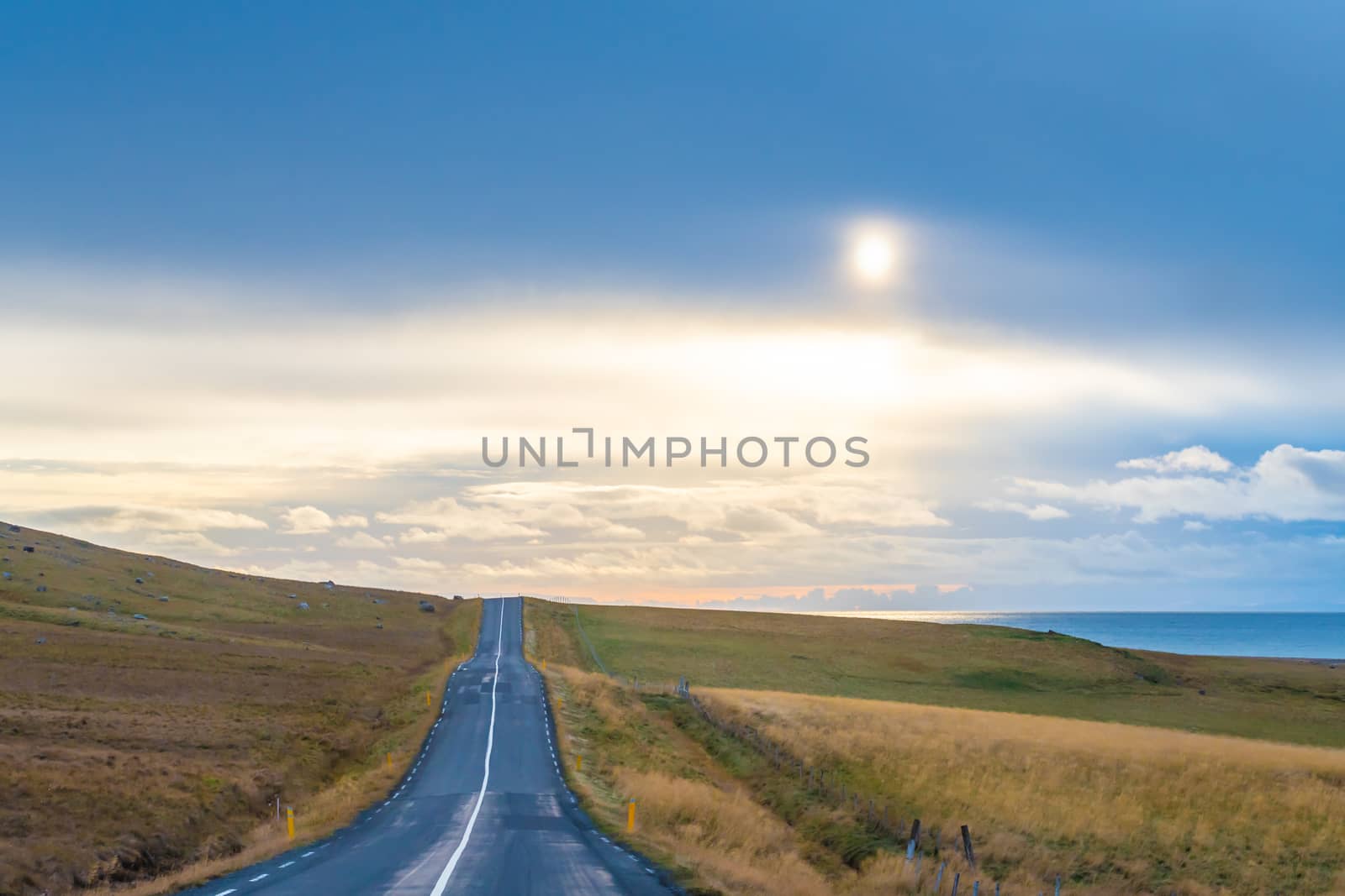 Road trip in Iceland empty road pointing into clearing sky colored yellow by sun