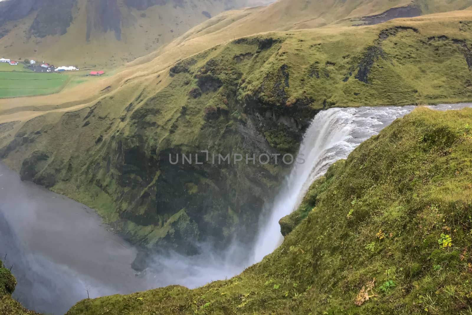 Skogafoss waterfall in Iceland top of waterfall during heavy rainfall between green rocks by MXW_Stock