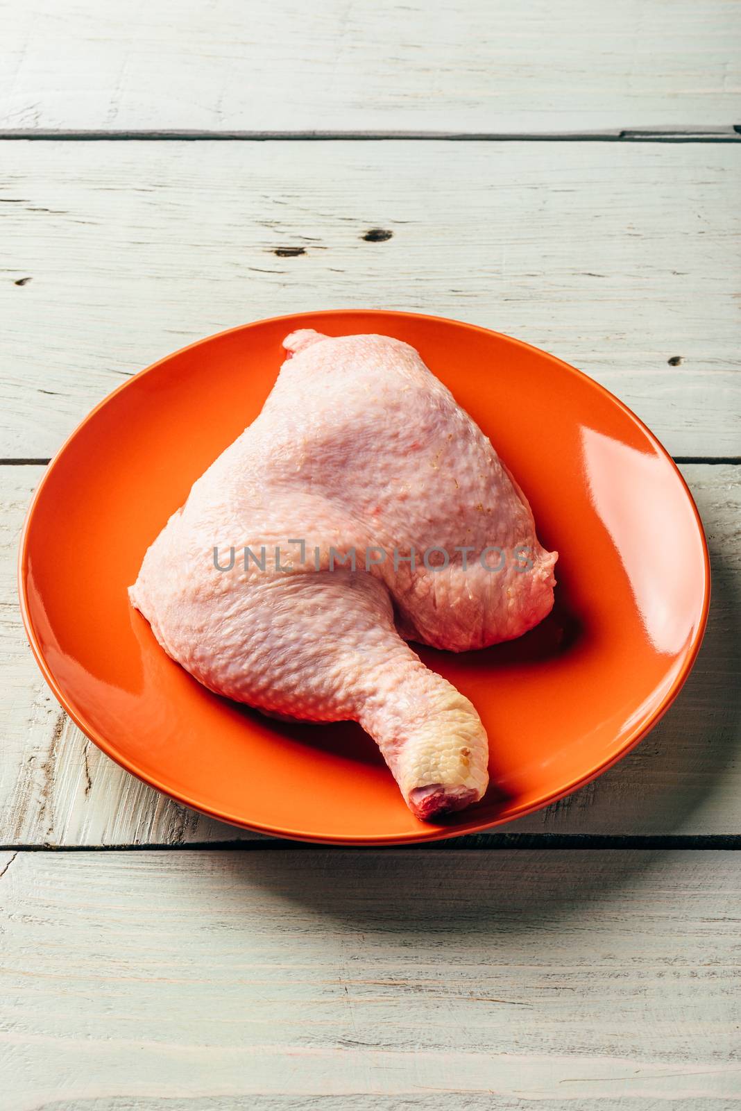 Chicken leg on orange plate over light wooden table