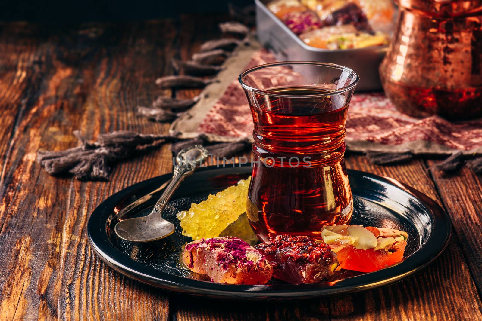 Tea in armudu glass with oriental delight rahat lokum on metal tray over wooden surface and tablecloth