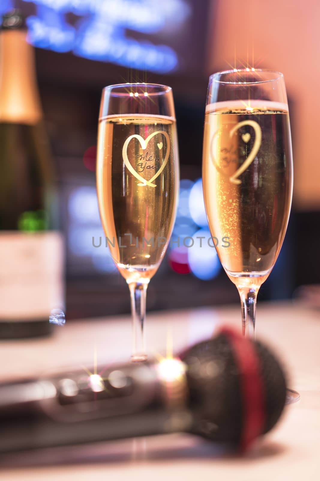 Black microphone in karaoke club, with champagne wine bottle and couple sparkling glass with heart shape and screen in background for singing music on stage party. 