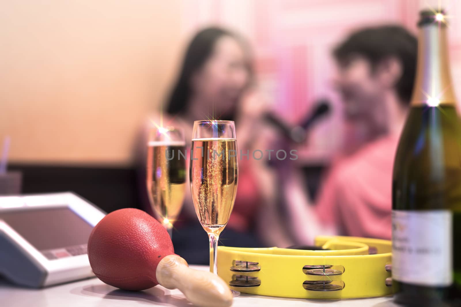 Red maraca in karaoke club, with champagne bottle and couple of sparkling wine glasses, yellow tambourine and screen for singing music on romantic stage party. 