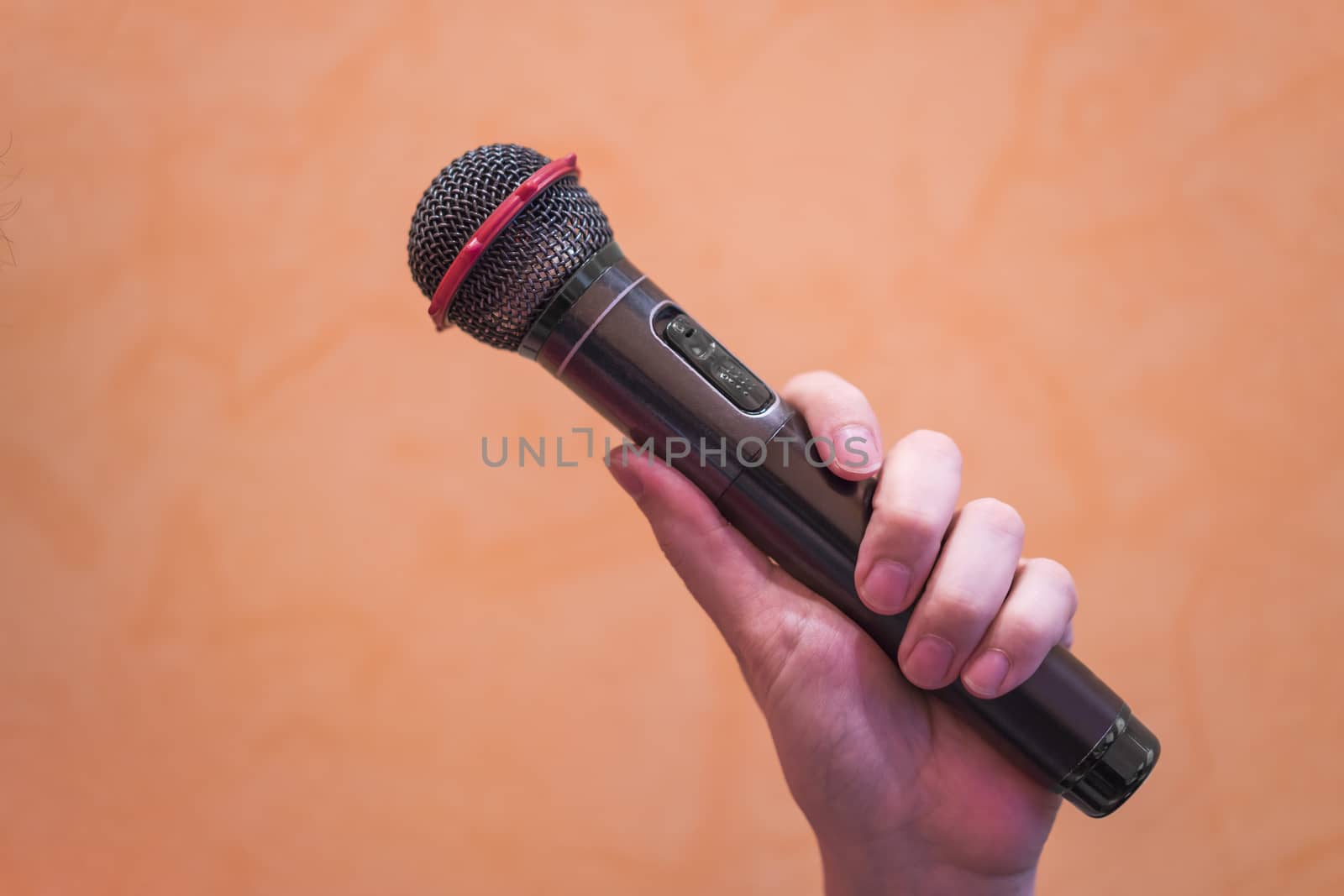 Close-up of a man's hand holding a black microphone on an orange background.
