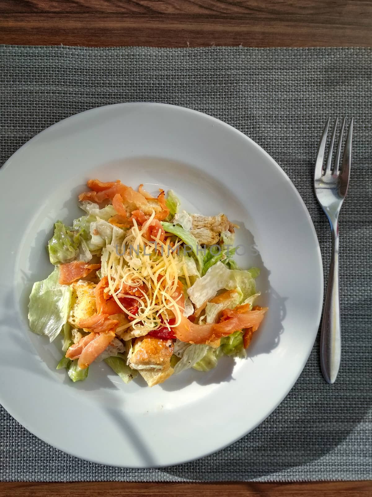 Ceasar salad with prosciutto ready-to-eat. Top view. Vertical. Ceasar salad on white plate on restaurant tabletop. Natural trendy hard daylight