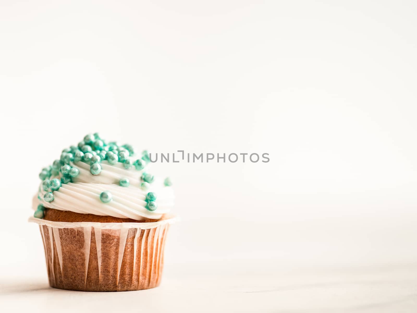 Cupcake decorated blue sprinkles and copy space right. White marble background.