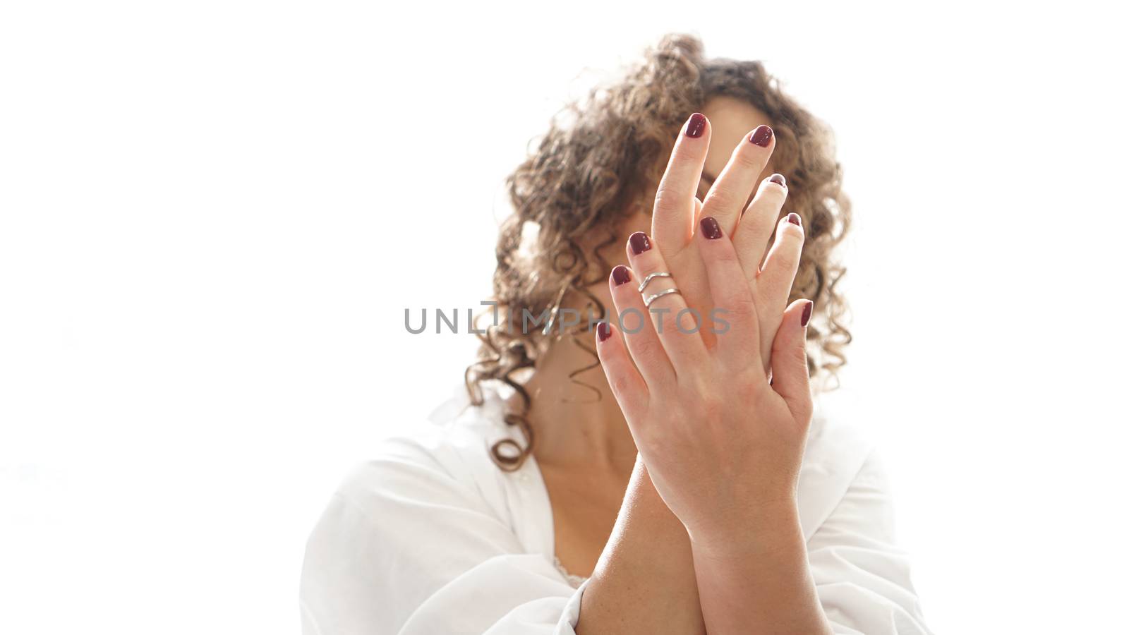 Closeup of hands of a young woman with dark red manicure on nails in front of face against white background
