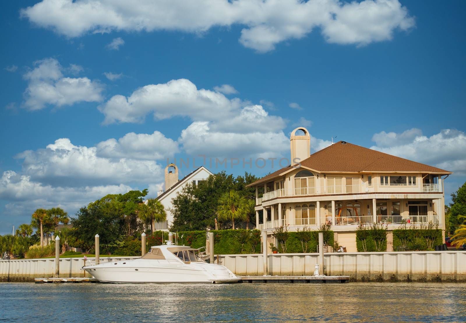 A nice three story home on a channel with a small white yacht anchored at dock