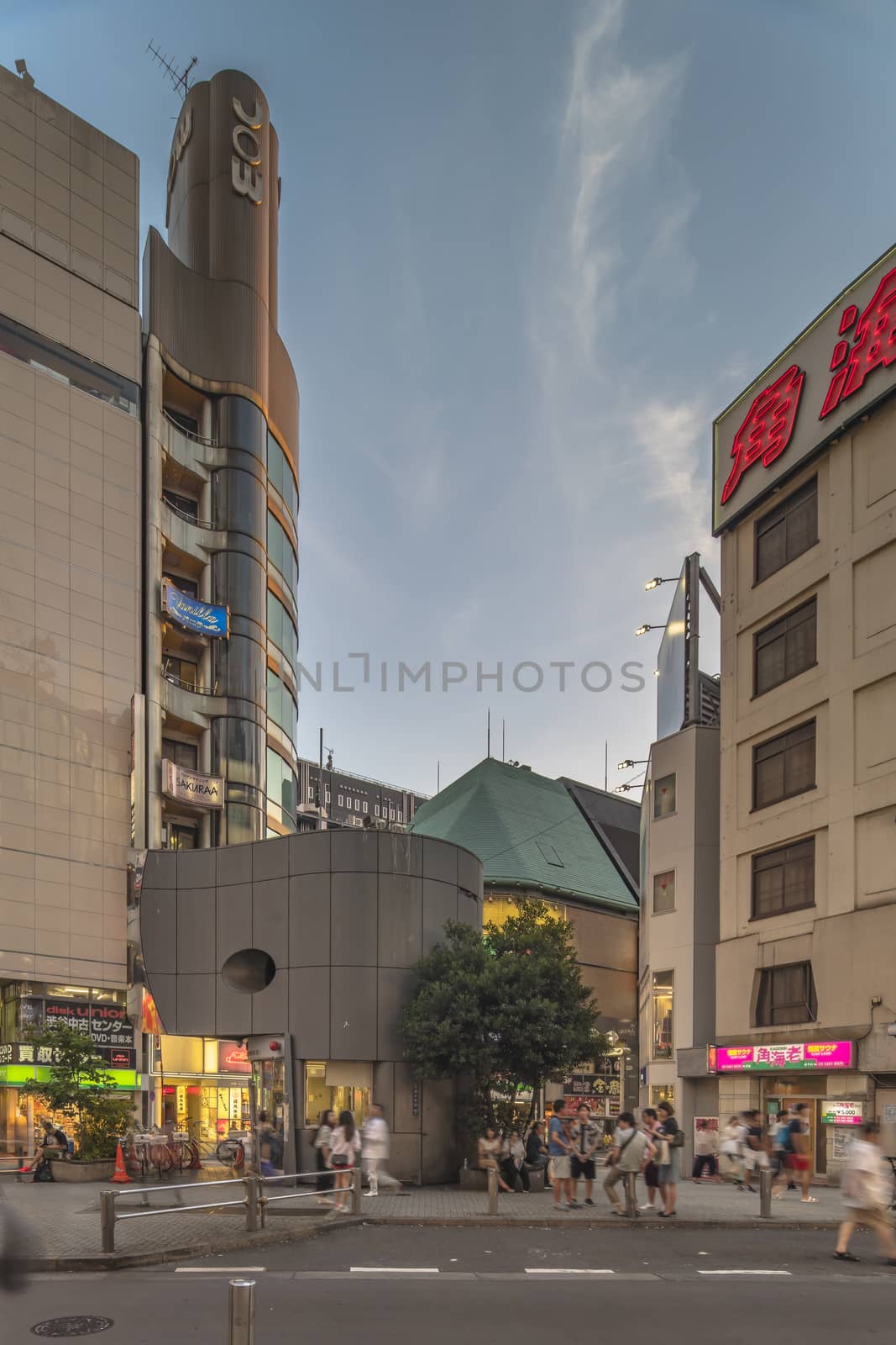 Sunset sky on owl iron mask Shaped of Shibuya Police Station Udagawa Kōban designed by architect Edward Suzuki and opened in April of 1985 in the Inokashira Steet of Shibuya Center Gai which literally means Shibuya Central District. The busiest street once intersected with Shibuya Station, it stretches for 350 meters and incorporates the adjacent streets of Bunkamura, Inokashira and Utagawa into its neighborhood. In 2011 the street was renamed Basketball Street in reference to the holy place of Japanese basketball which is the Yoyogi National Gymnasium to which this street leads. The photo is taken in summer at the Tanabata Star Festival where the portal is adorned with paper decorations in the shape of shooting stars for the occasion.