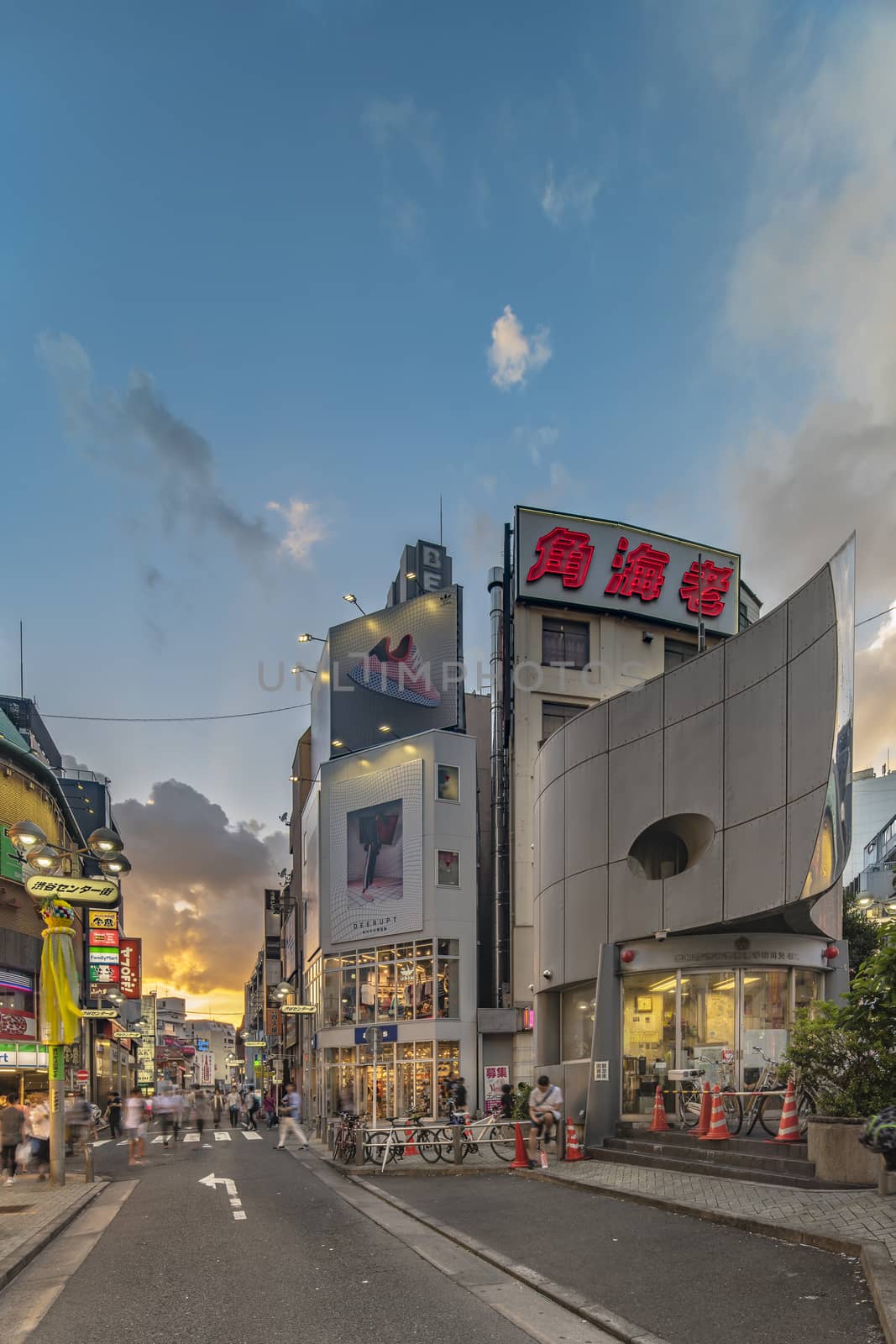 Sunset sky on owl iron mask Shaped of Shibuya Police Station Udagawa Kōban designed by architect Edward Suzuki and opened in April of 1985 in the Inokashira Steet of Shibuya Center Gai which literally means Shibuya Central District. The busiest street once intersected with Shibuya Station, it stretches for 350 meters and incorporates the adjacent streets of Bunkamura, Inokashira and Utagawa into its neighborhood. In 2011 the street was renamed Basketball Street in reference to the holy place of Japanese basketball which is the Yoyogi National Gymnasium to which this street leads. The photo is taken in summer at the Tanabata Star Festival where the portal is adorned with paper decorations in the shape of shooting stars for the occasion.